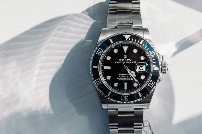 Ρολόι Rolex με μαύρο καντράν και μεταλλικό μπρασελέ σε μαρμάρινη επιφάνεια